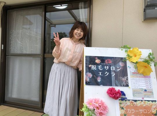 サロン入口の前に立て看板と代表が立っている写真